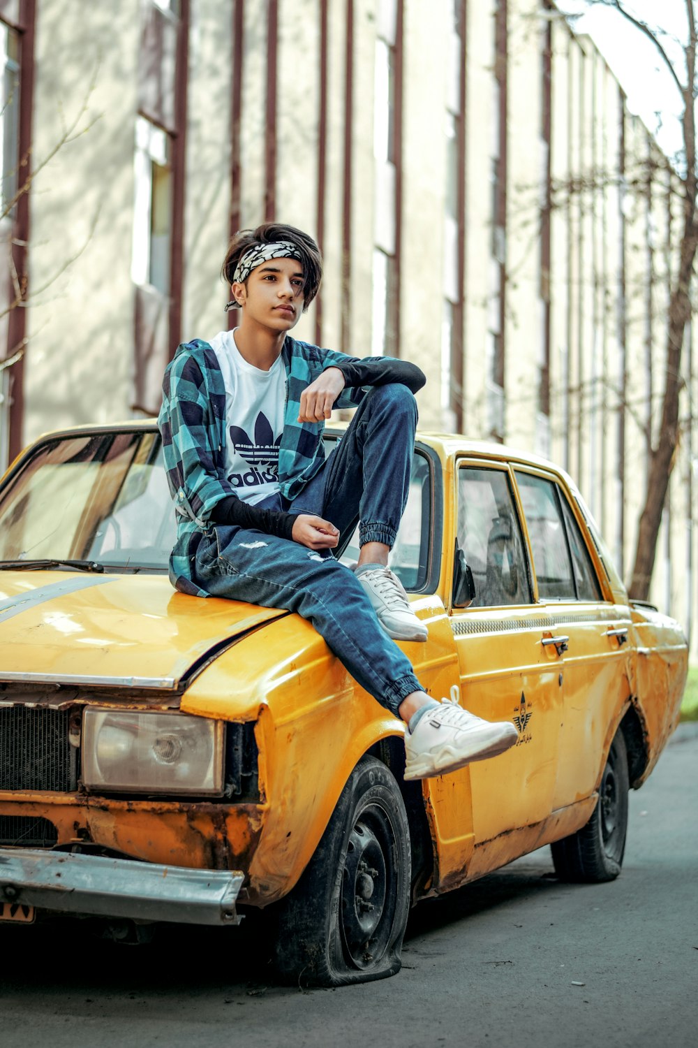 man in blue and white jacket and blue denim jeans sitting on yellow car