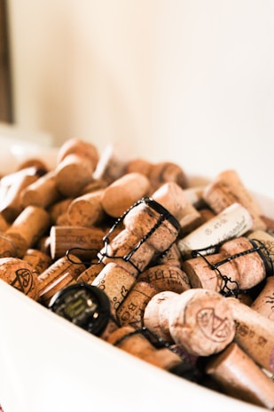 A collection of champagne corks and wire cages is gathered in a white container. The corks are of various brands and inscriptions, suggesting they have been collected over time.