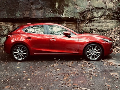A shiny red hatchback on a city street with autumn leaves around.