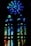A stained glass window featuring a large circular pattern at the top and a series of elongated vertical and smaller circular segments below. The glass is intricately designed with a mosaic of blue, green, and hints of red and yellow colors that blend beautifully together.