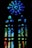 A stained glass window featuring a large circular pattern at the top and a series of elongated vertical and smaller circular segments below. The glass is intricately designed with a mosaic of blue, green, and hints of red and yellow colors that blend beautifully together.