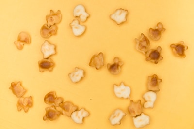 A collection of small, biscuit-like snacks shaped like various animals, scattered across a yellow surface. The snacks have a light brown and golden color, some darker than others, suggesting varying levels of baking.