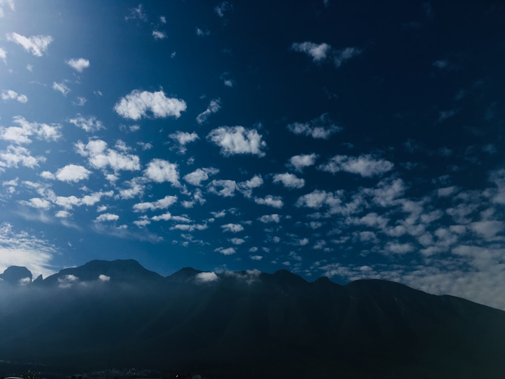 silhouette of mountains under blue sky and white clouds during daytime