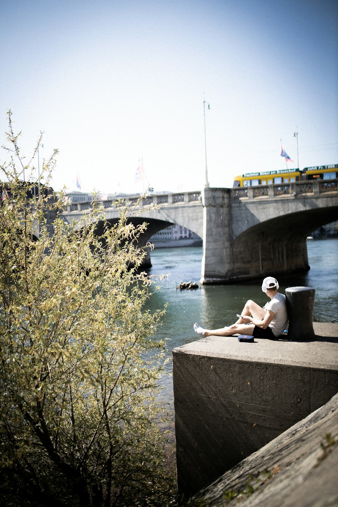 woman in white tank top sitting on concrete bridge over river during daytime