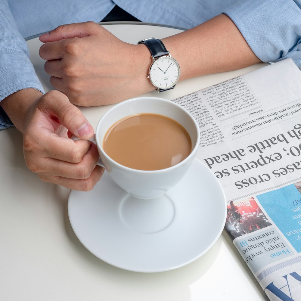 Persona en camisa azul de manga larga sosteniendo una taza de cerámica blanca con líquido marrón