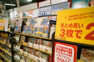 A music store shelf is filled with various CDs, focusing on a section labeled 'Japanese City Pop.' The area is well-organized with different discs prominently displaying labels such as 'Disc 1,' 'Disc 2,' and 'Disc 3.' Promotional signage in Japanese is visible, offering discounts. Headphones and numerous CD covers are present, creating a vibrant and busy atmosphere.