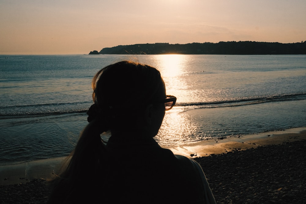 silhouette of woman standing near body of water during sunset