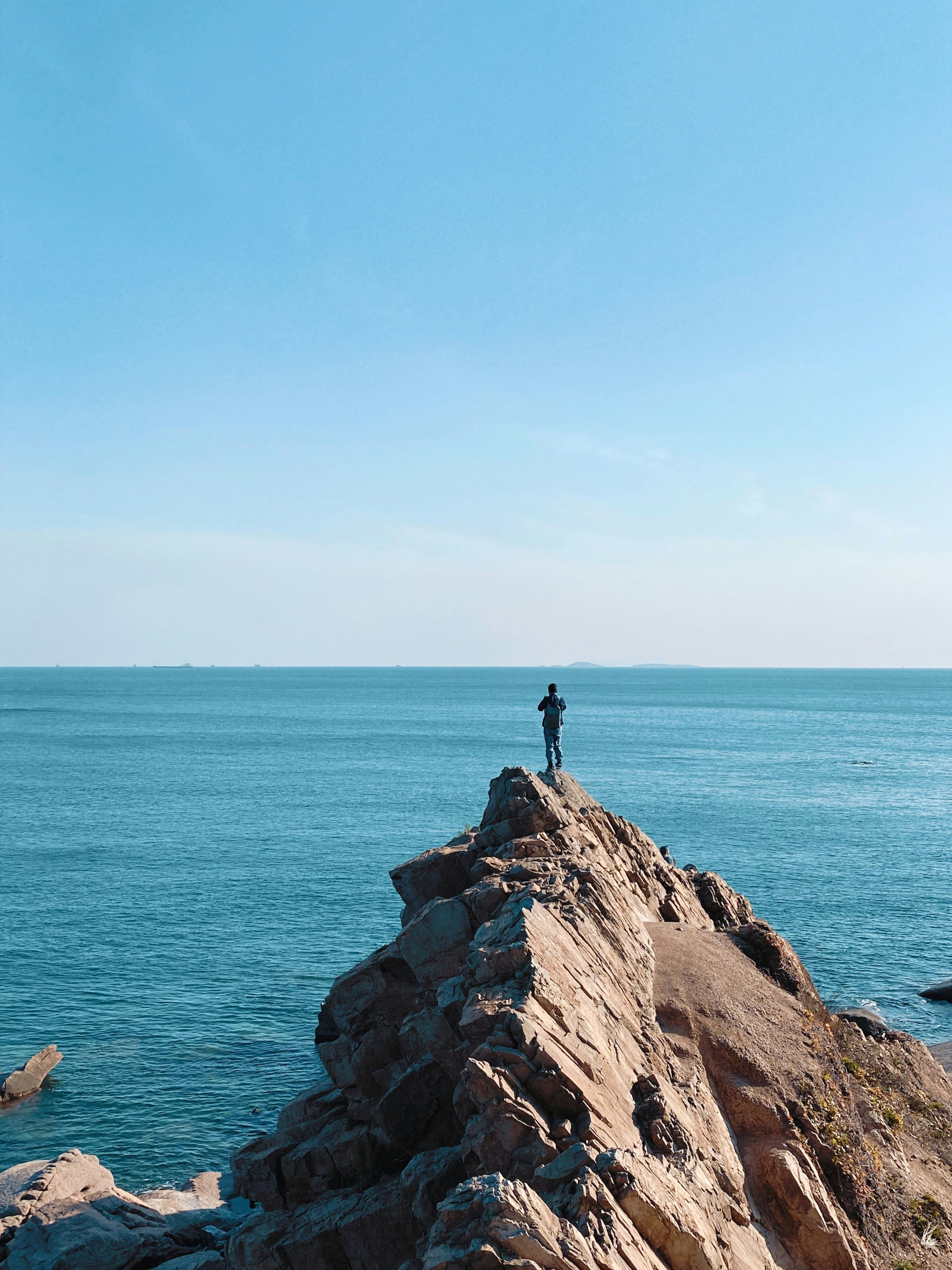 person standing on rock formation near sea during daytime