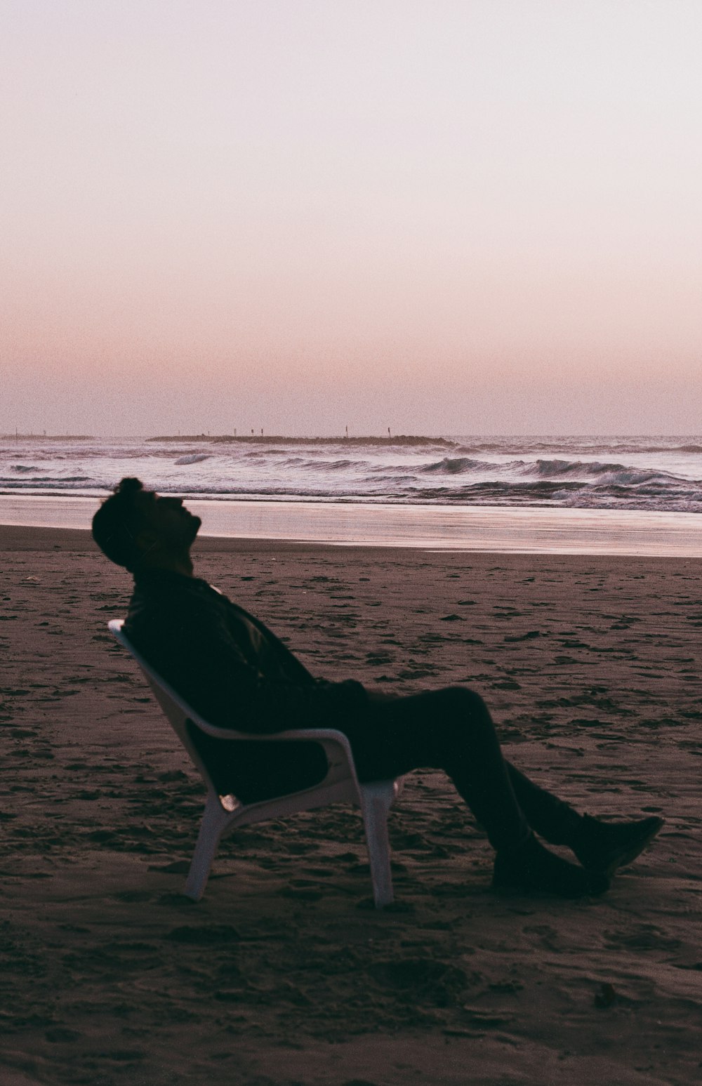 silhouette of person sitting on white plastic chair on beach during daytime