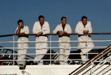 4 men in white dress shirt standing on white boat during daytime