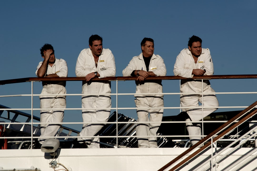 4 men in white dress shirt standing on white boat during daytime
