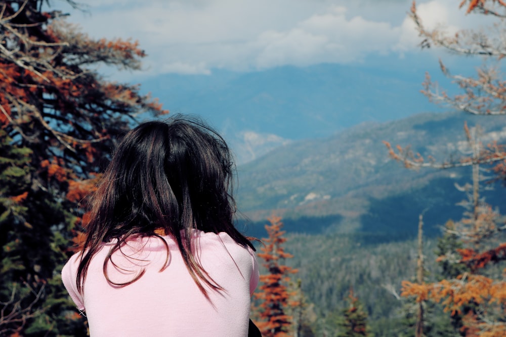 woman in pink shirt standing near brown and green trees during daytime