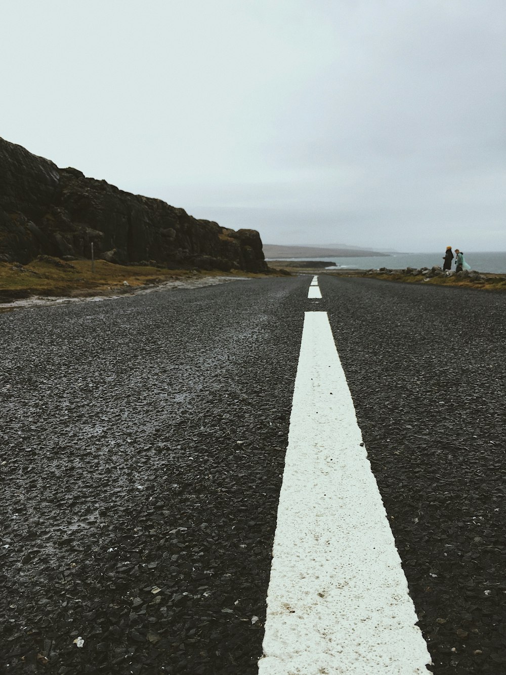 gray concrete road between brown and green mountain under white clouds during daytime