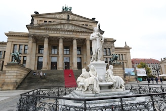 A grand architectural building with classical design elements such as large columns and statues. The building is adorned with stone sculptures and a red carpet on the stairs. The structure is likely a cultural or historical landmark.