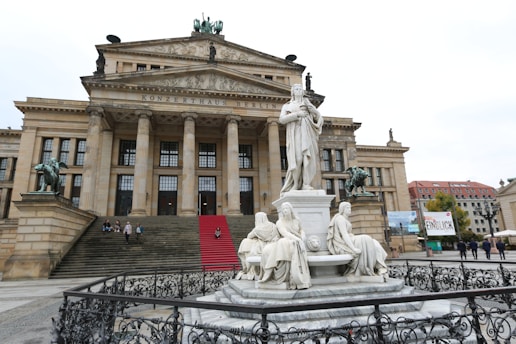 A grand architectural building with classical design elements such as large columns and statues. The building is adorned with stone sculptures and a red carpet on the stairs. The structure is likely a cultural or historical landmark.