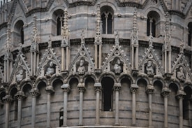 Intricate stone carvings and sculptures adorn an ornate facade, with numerous arches and arches topped by geometrical designs. Statues of figures are placed between the arches, conveying a sense of historical craftsmanship and artistry.