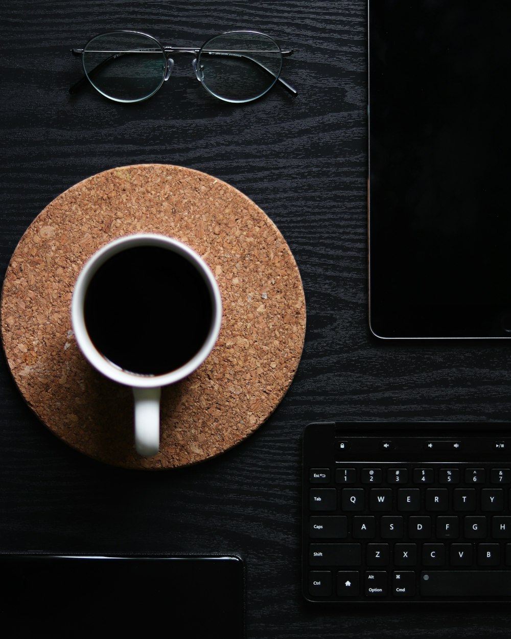 white ceramic mug beside black framed eyeglasses on brown wooden table