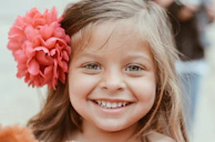 A cheerful girl with pastel pink braided hair styled with small pearl clips, smiling outdoors.