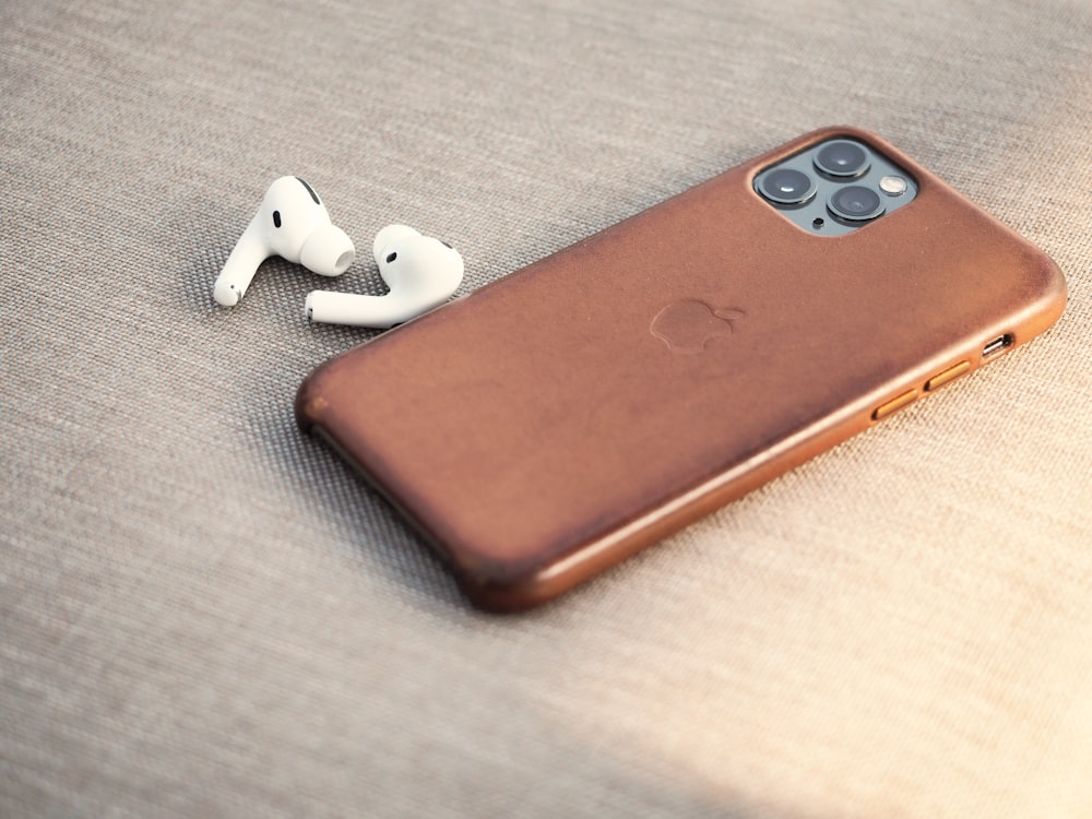 brown leather smartphone case beside white earbuds