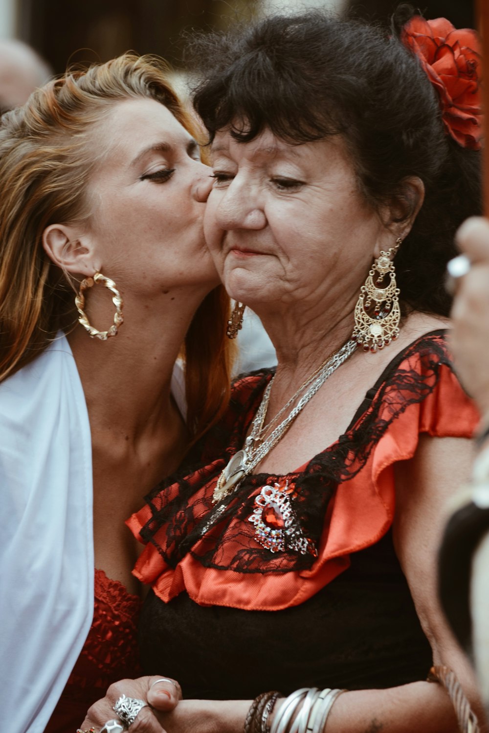 Frau in rotem und schwarzem Blumenkleid küsst Frau in weißem Kleid