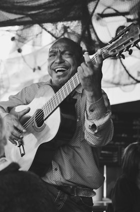 A joyful person playing cavaquinho surrounded by classic samba sheet music in a cozy home setting