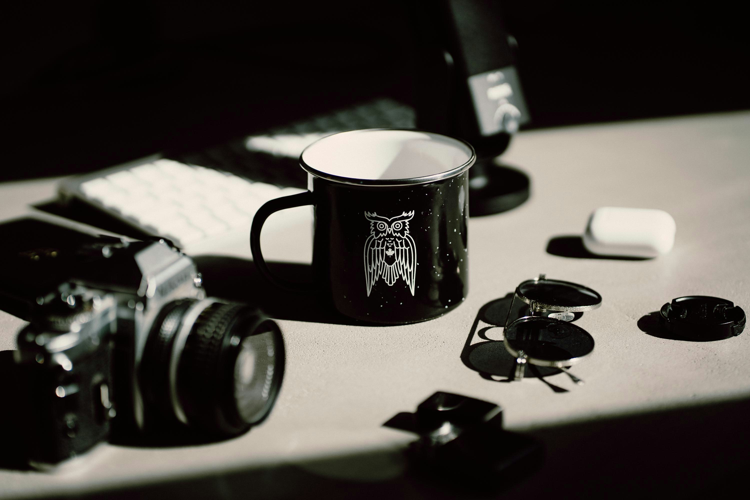 black and white ceramic mug beside black and silver dslr camera on white table