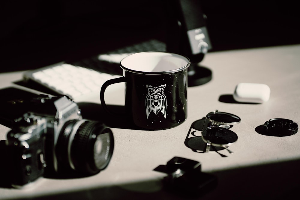 black and white ceramic mug beside black and silver dslr camera on white table