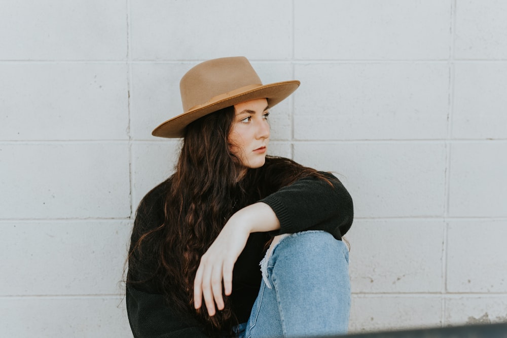 woman in black long sleeve shirt and blue denim jeans wearing brown hat sitting on white