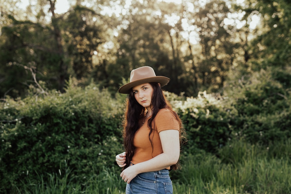 woman in brown hat and orange shirt standing on green grass field during daytime