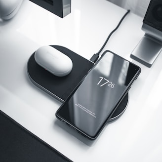 A sleek modern smartphone and wireless earbuds displayed on a minimalist desk.