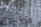 A textured concrete wall with a weathered and aged appearance, showing various shades of gray and black with subtle hints of white. The surface is marked by rough patches, cracks, and stains, giving it a rugged, industrial feel.