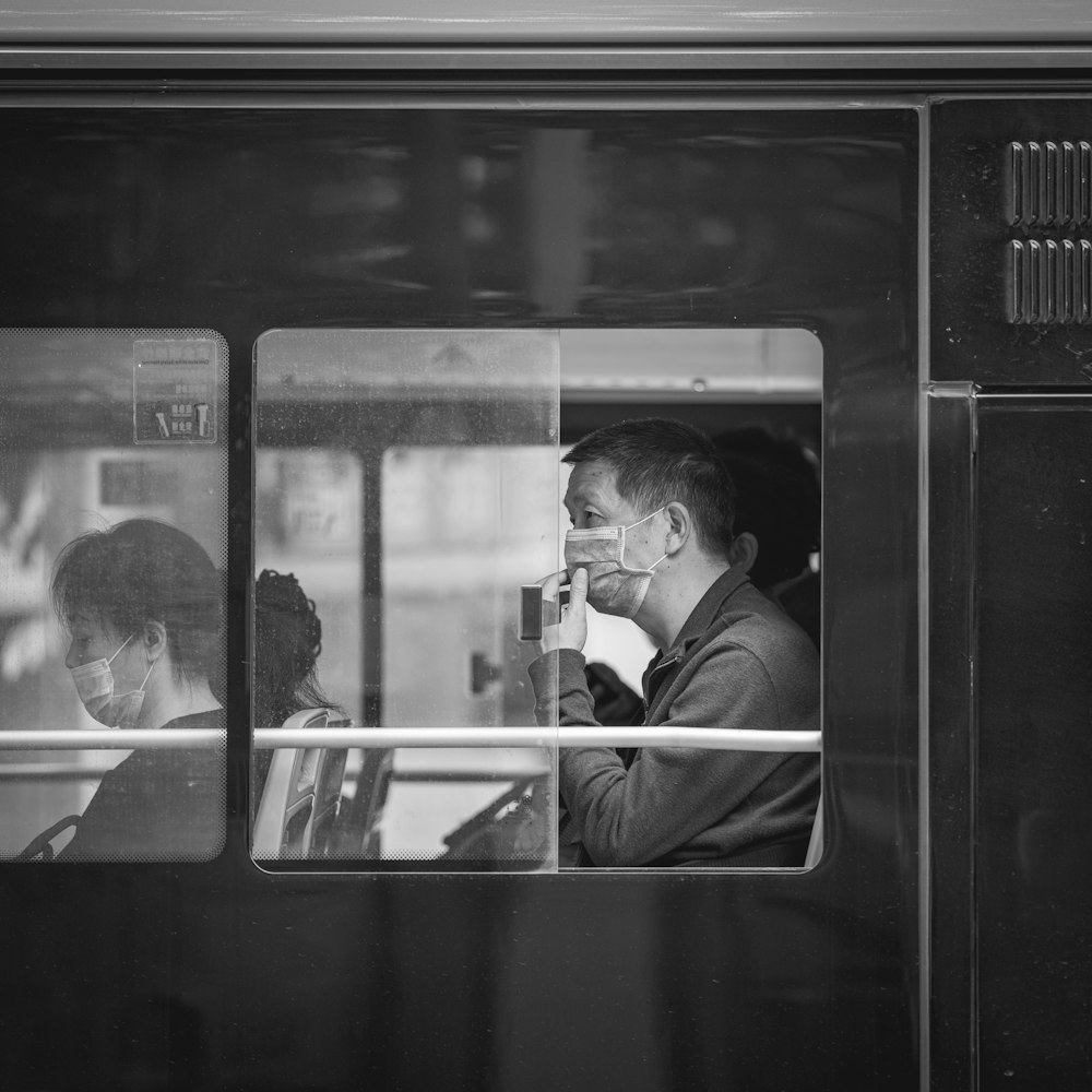 grayscale photo of man in jacket sitting on train