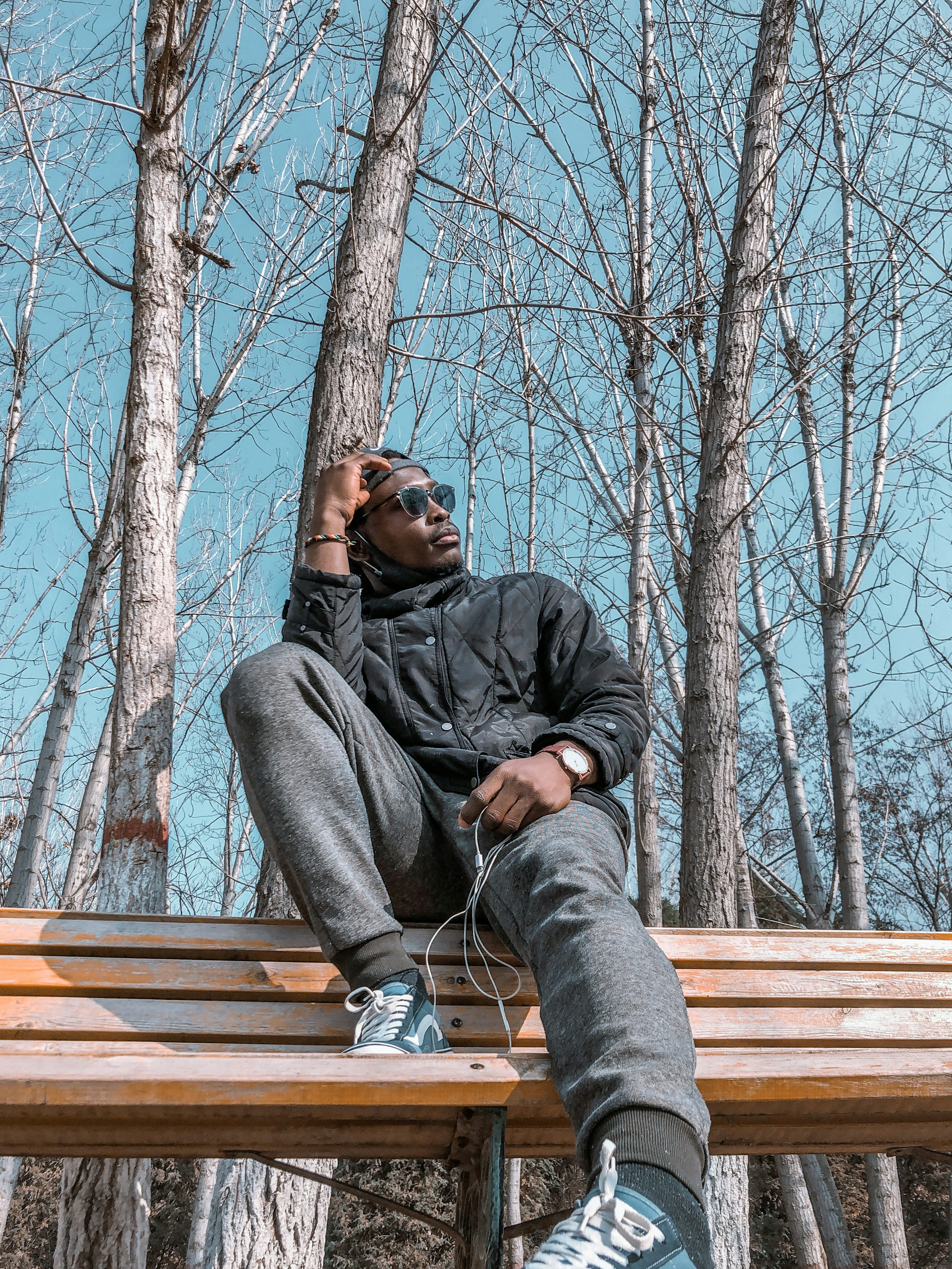 man in black jacket and gray pants sitting on brown wooden bench