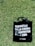 A black tote bag with white text in Spanish on one side is placed on a patch of vibrant green grass. The text reads 'DISFRUTAR DE LA COMIDA ES DISFRUTAR DE LA VIDA' with 'LA-MERA' written at the bottom.