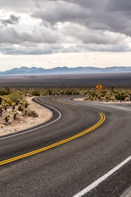 gray concrete road near green trees under white clouds during daytime