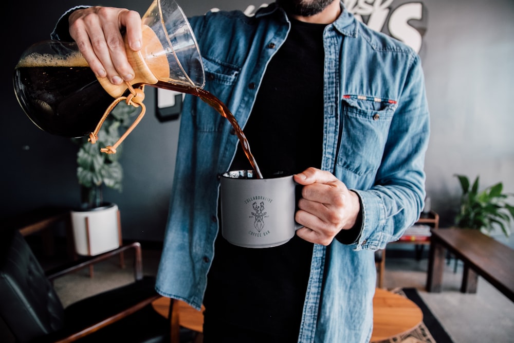 man in blue denim jacket holding white ceramic mug