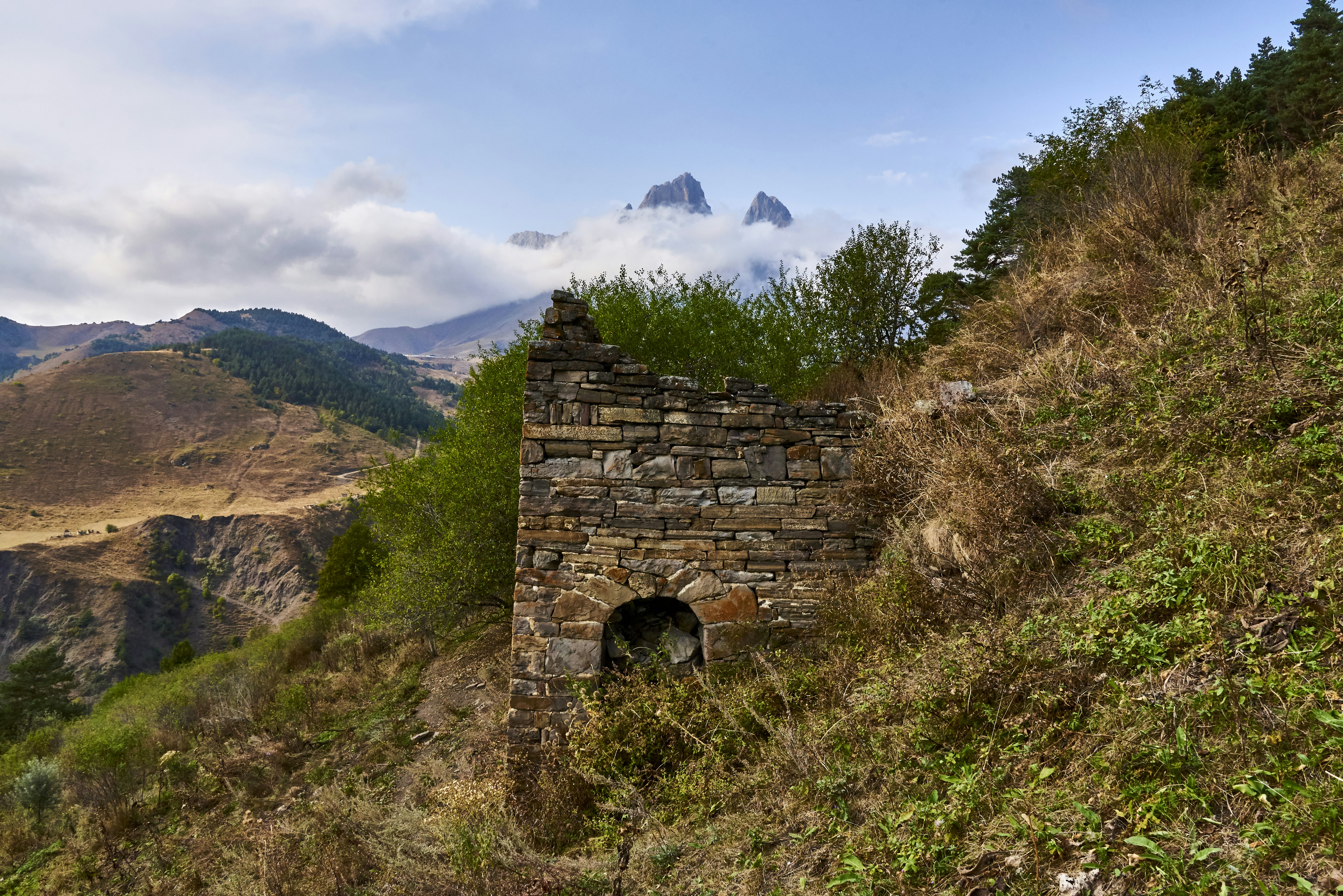 brown brick wall on green grass field near mountain under white clouds and blue sky during