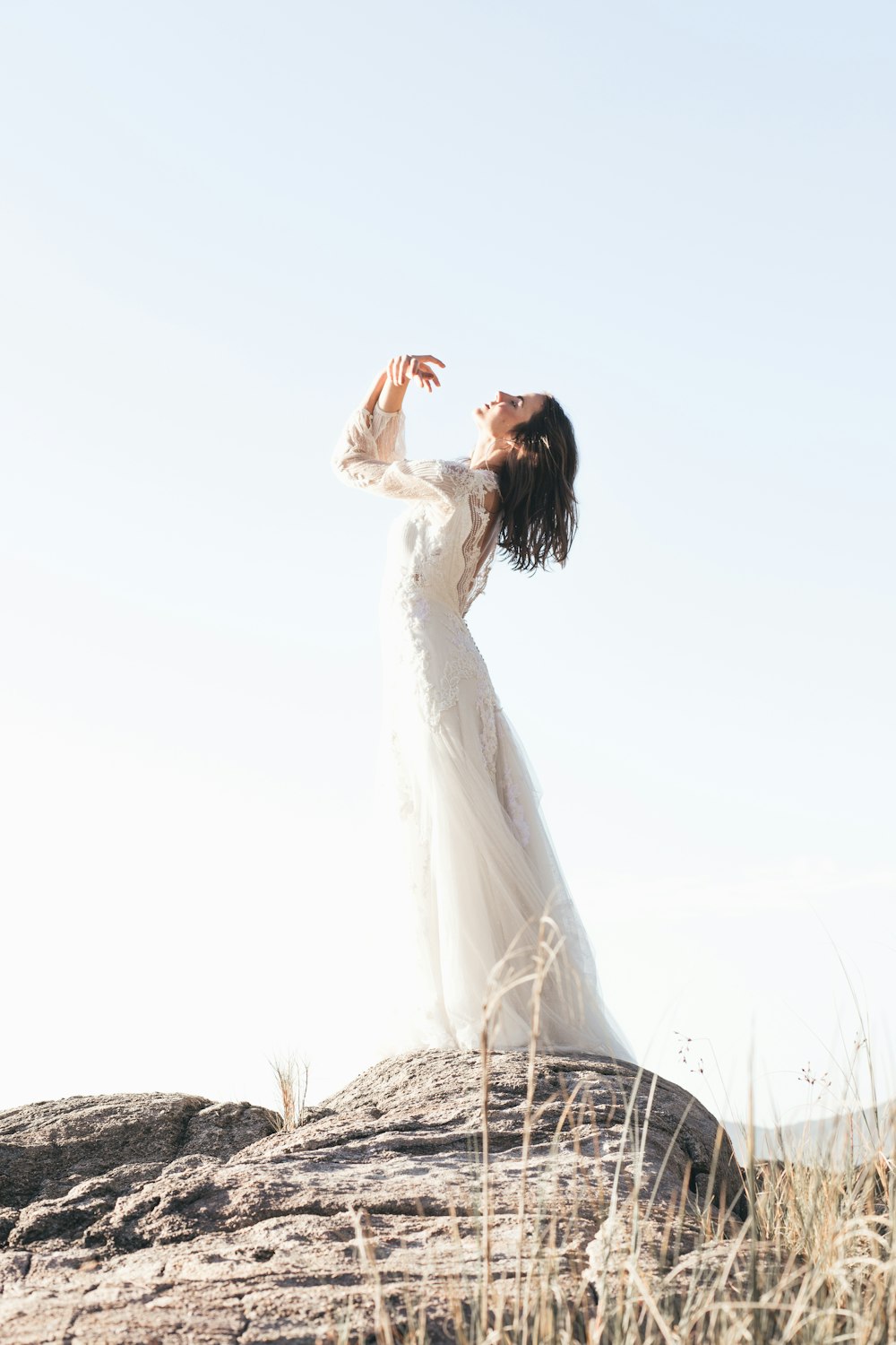 femme en robe de mariée blanche debout sur le champ d’herbe brune pendant la journée
