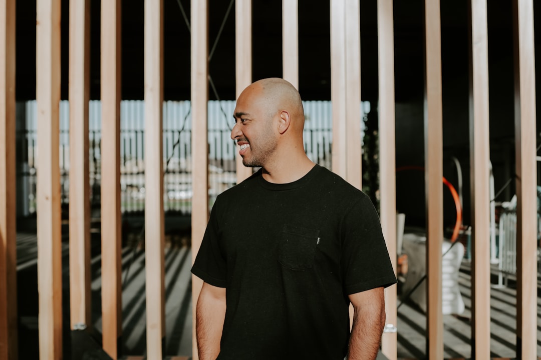 man in black crew neck t-shirt standing near brown metal gate during daytime