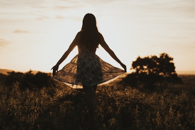 Sunset silhouette of a flamenco dancer with flowing dress in an open field.