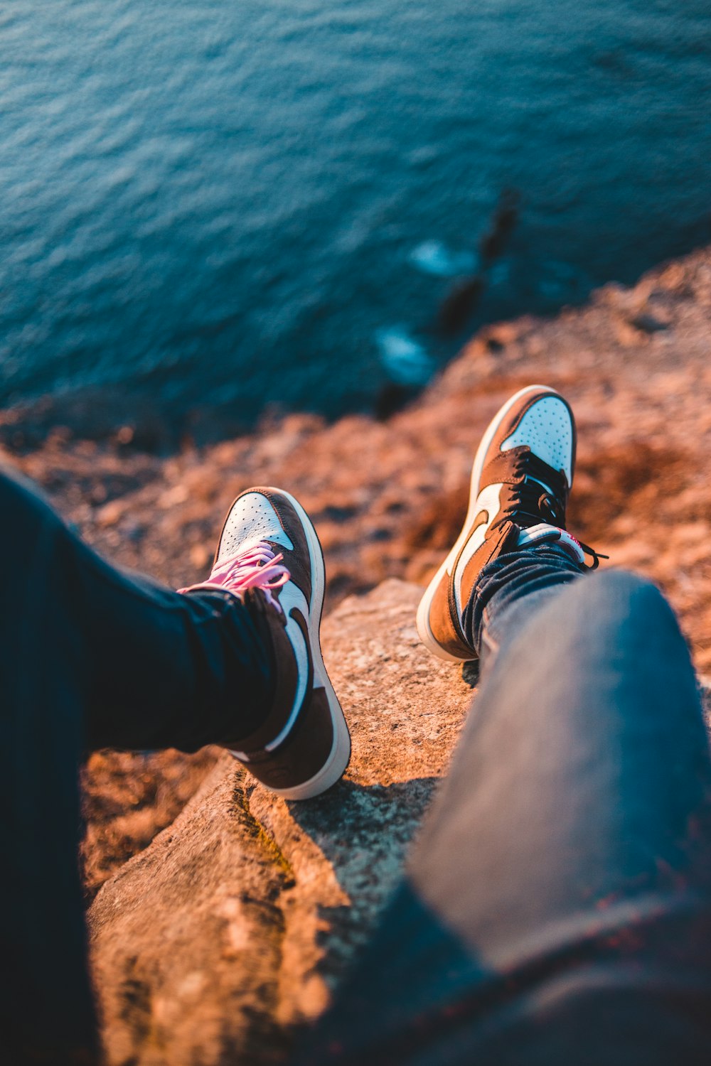 person in black pants and brown and white sneakers sitting on brown rock near body of near near near near