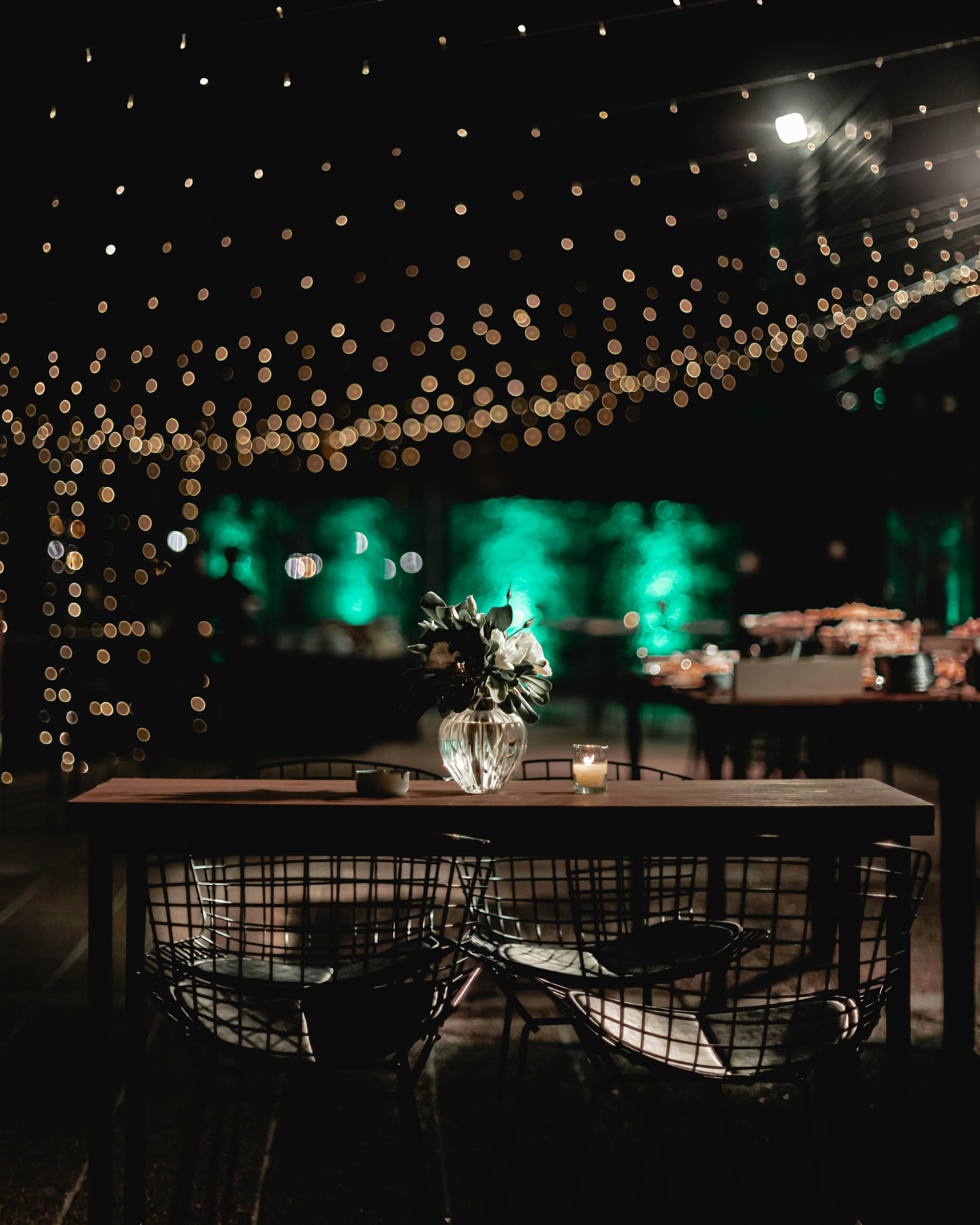 An inviting outdoor dining setup with a table set for a meal, surrounded by greenery and warm lighting.