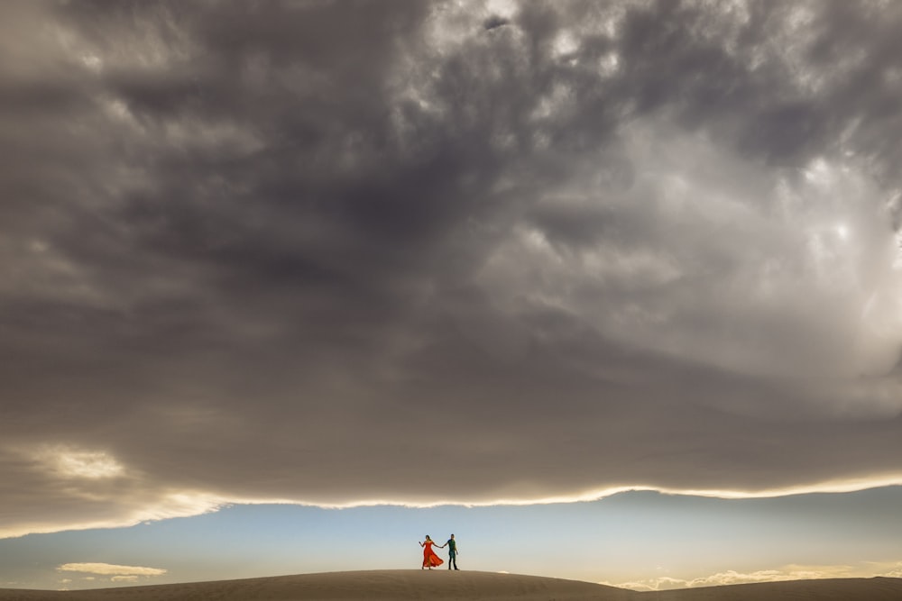 silhouette of person standing on top of hill under cloudy sky during daytime