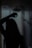 A silhouette of a person is visible behind a fogged-up glass shower door, with some streaks and droplets on the glass. The scene is dimly lit, adding a mysterious or introspective atmosphere.