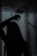 A silhouette of a person is visible behind a fogged-up glass shower door, with some streaks and droplets on the glass. The scene is dimly lit, adding a mysterious or introspective atmosphere.