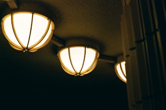 Three spherical ceiling lights with a warm glow illuminate a textured ceiling. The lights are encased in a decorative metal grid, suggesting an industrial or vintage style. The setting appears dim, enhancing the focus on the glowing lights.
