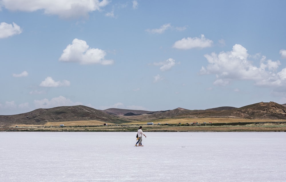 person in white shirt and black pants walking on white sand beach during daytime