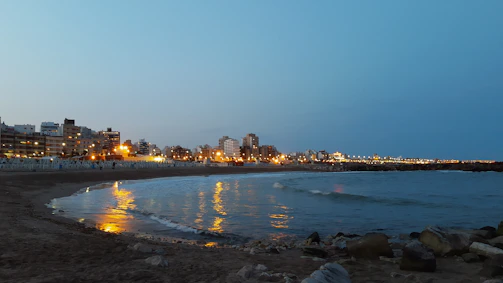 A coastal city skyline at dusk with soft golden light reflecting on water.