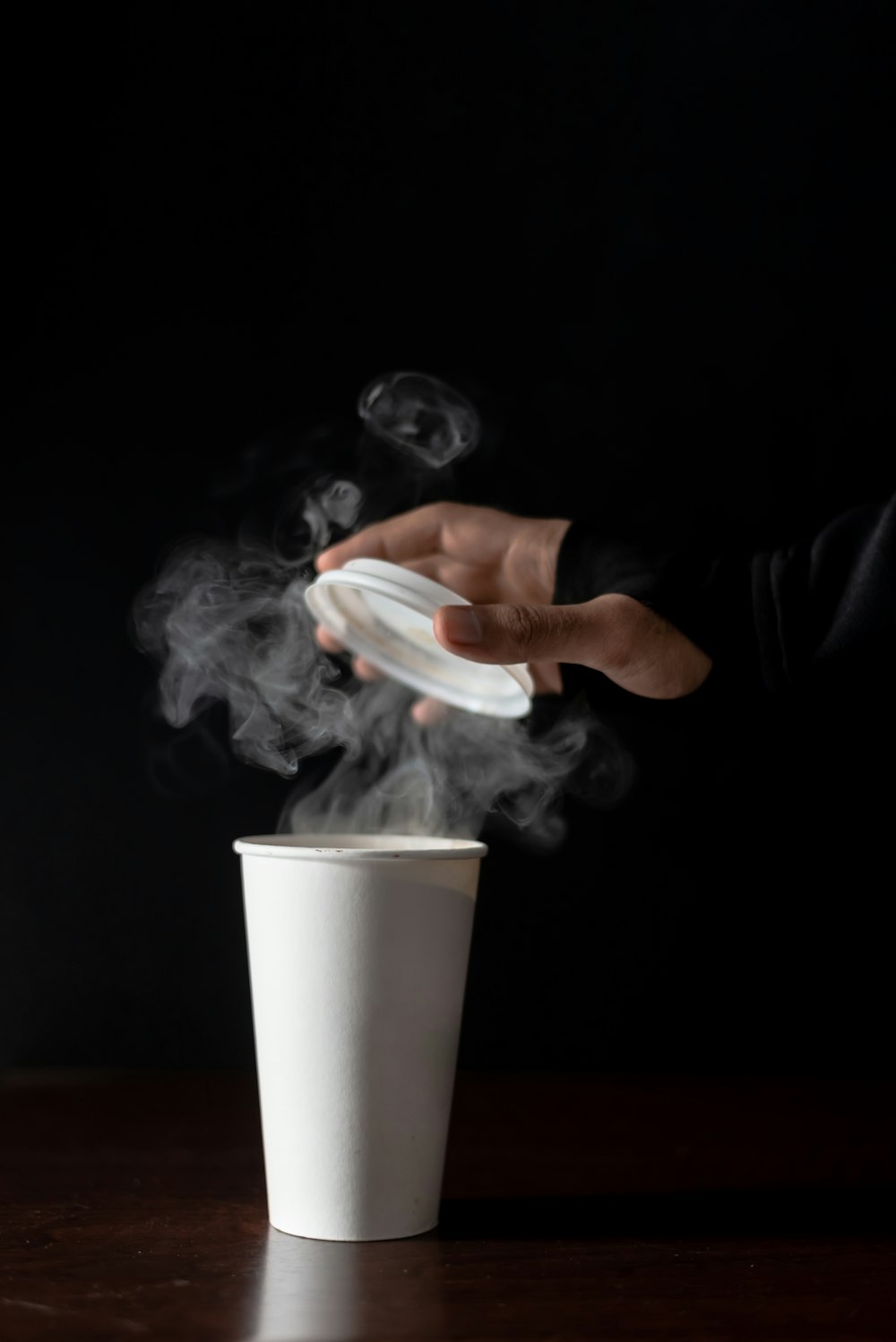 person holding white disposable cup with white smoke