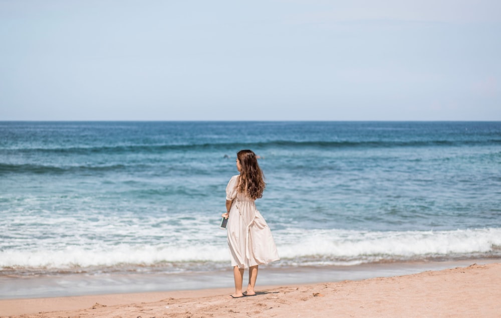 donna in abito bianco in piedi sulla spiaggia durante il giorno